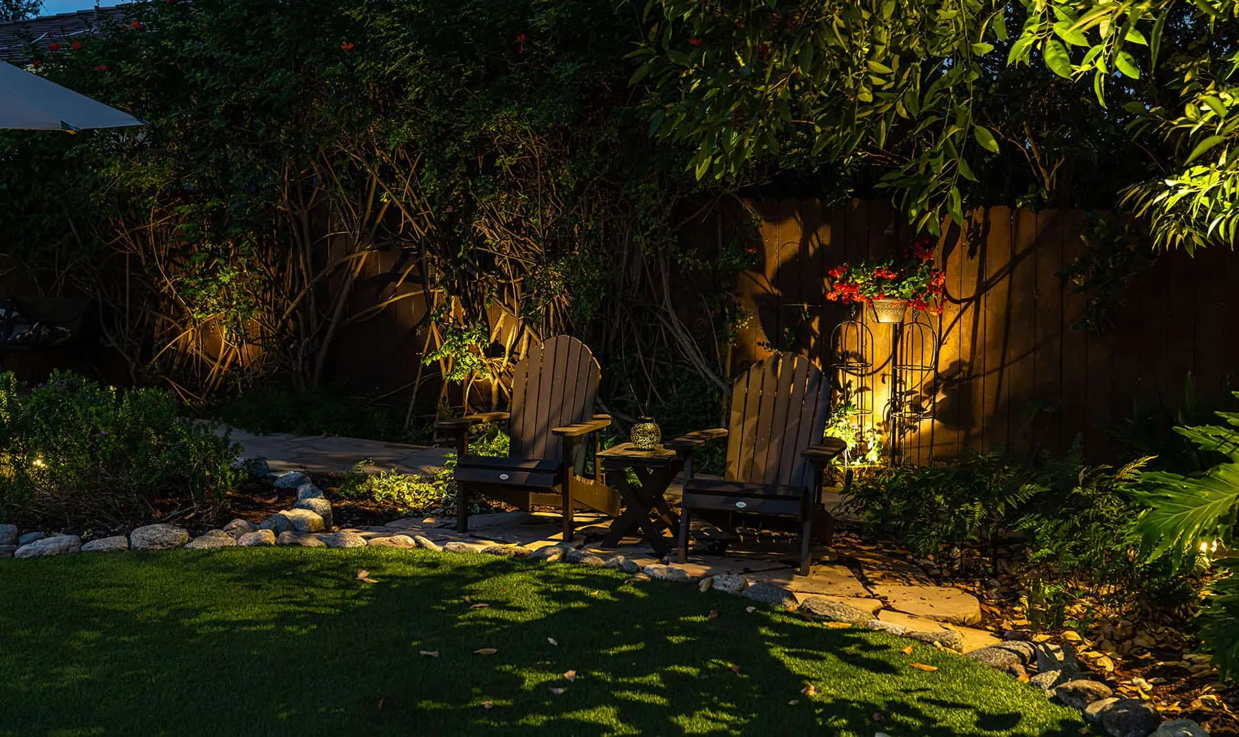 Dimmable backyard landscape lighting around seating, shrubs, and fence line for an outdoor living space in Charleston SC