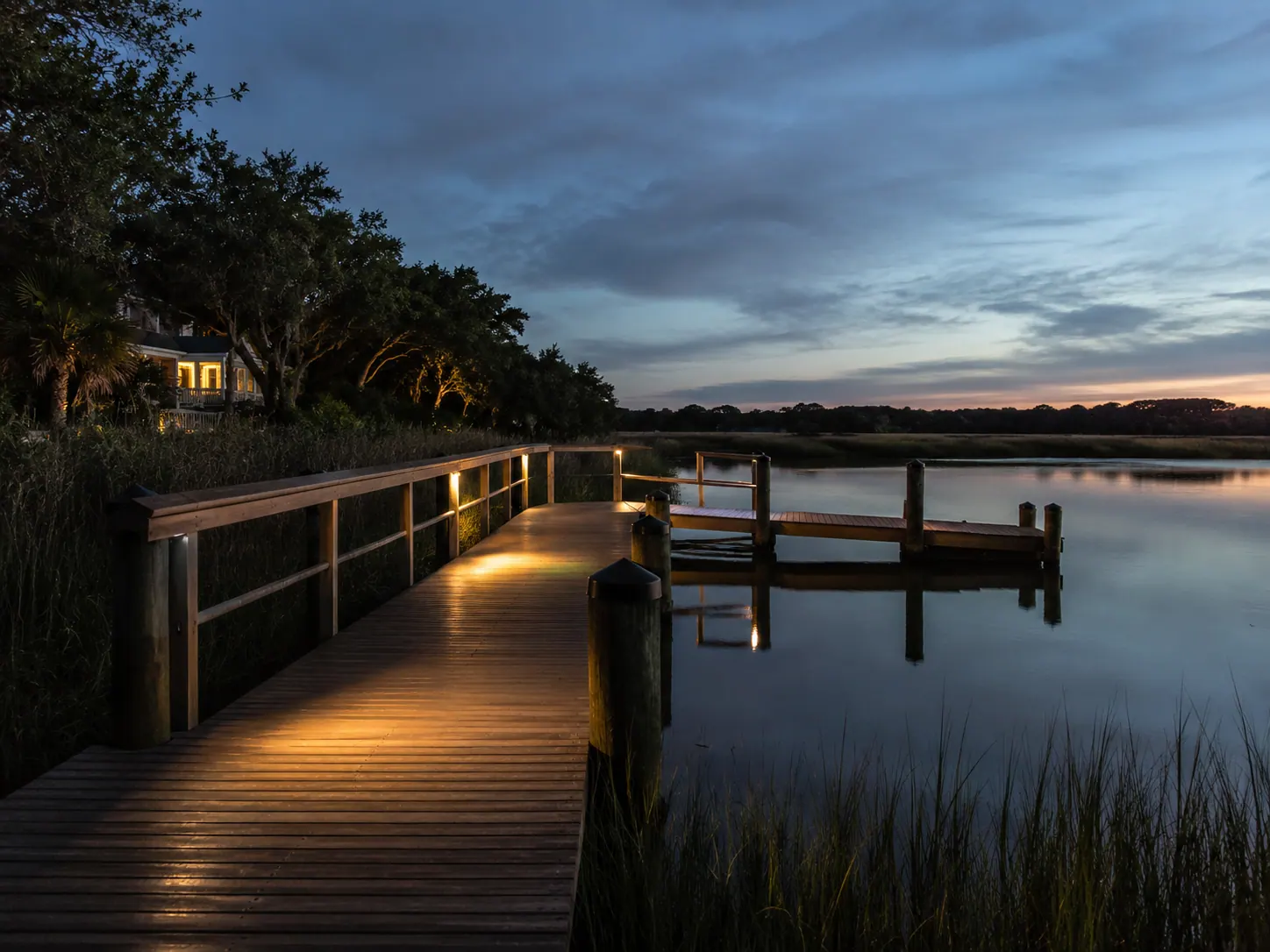 Dock lighting along a Charleston marsh walkway at dusk with warm low voltage lights on the railings and deck