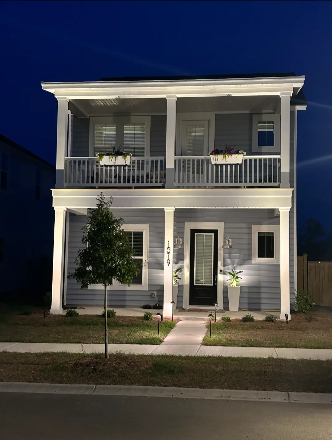 Illuminated two story Lowcountry home with warm pillar lighting and landscape lighting at night