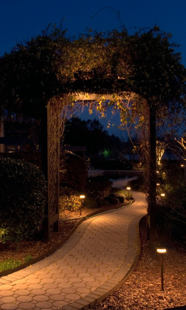 Low voltage path lights along a curved brick garden walkway under a vine covered arbor in Charleston SC